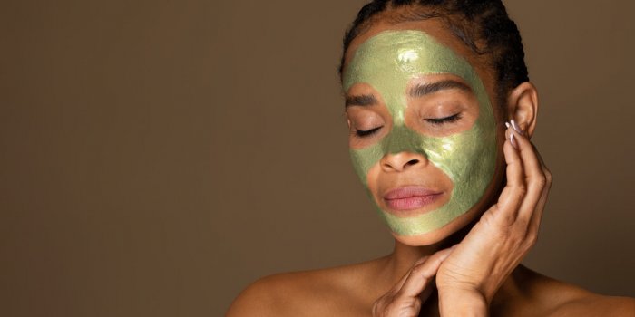 sensual african american middle aged woman with green peel-off mask on her face posing isolated on brown background, copy...