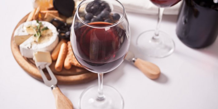 two glass of red wine and plate with assorted cheese, fruit and other snacks for party