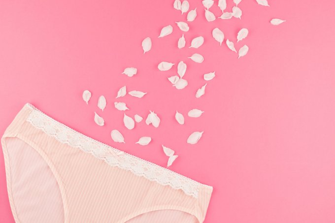 feminine flat lay set of female panties and white flowers petals on pastel pink color background for fashion blog and soc...