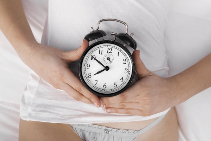 woman in white holding a black clock over her abdomen