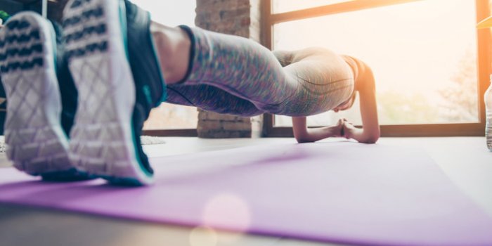 close up photo of sportswoman's sneakers athlete is holding plank position standing on elbows on purple carpet in class c...