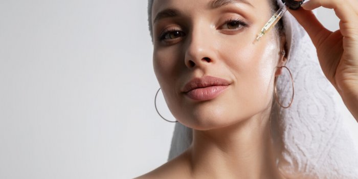 closeup studio portrait with young woman in bath towel on head isolated on copy space applying oil serum from pipette nat...