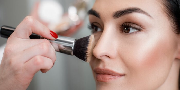 close up of makeup artist applying light layer of matting powder while using professional brush for lady