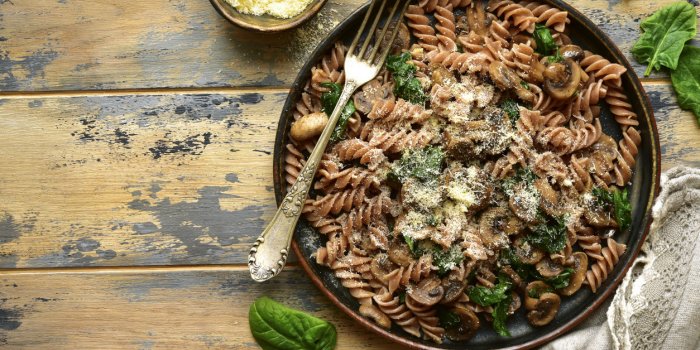 whole wheat fusilli pasta with mushroom and spinach on a dark plate over old rustic wooden backgroundtop view with copy space