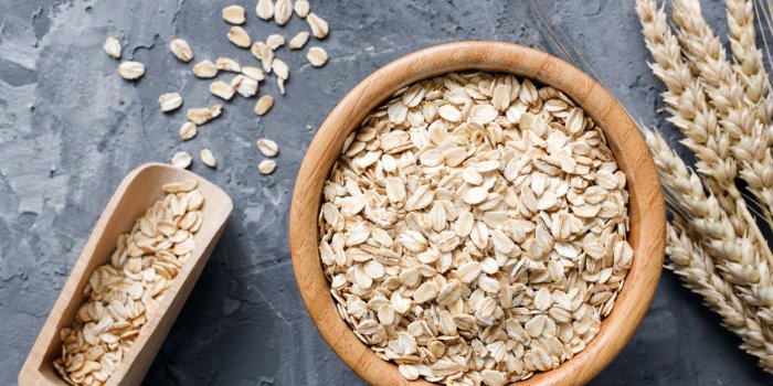 rolled oats or oat flakes in wooden bowl and golden wheat ears on stone background top view, horizontal healthy lifestyle...