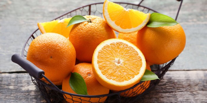 orange fruit with green leafs in basket on grey wooden table