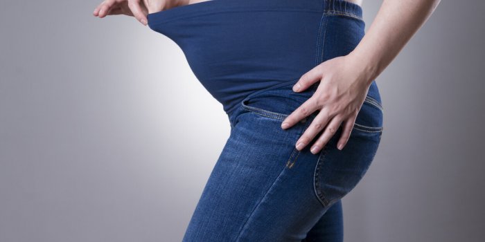 pregnant woman in blue jeans for pregnant women on gray background side view