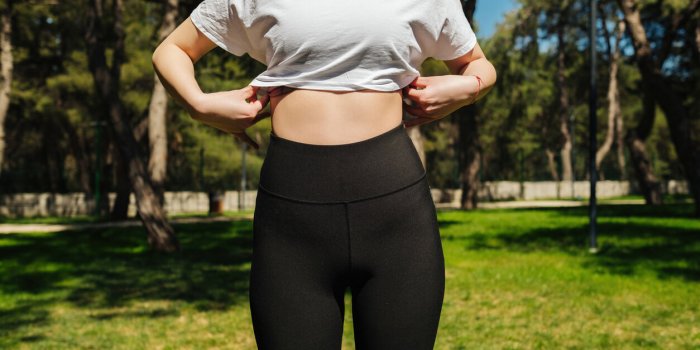 young sportive woman wearing black yoga pant and white tees standing on a park bench