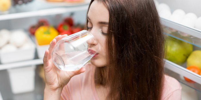 young woman drinking water near the refrigerator