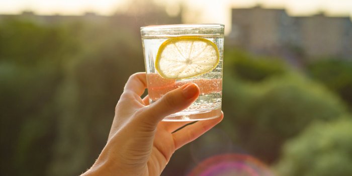 glass of clear, sparkling water with lemon in hand background sky, silhouette of the city, sunset