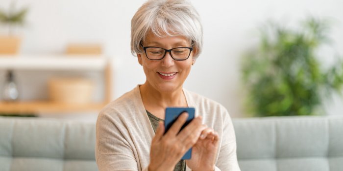 joyful beautiful senior woman is using smartphone sitting on the sofa at home