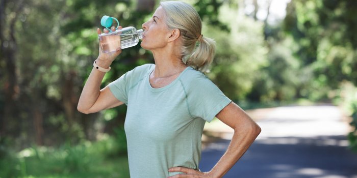 shot of a mature woman drinking water while exercising outdoors