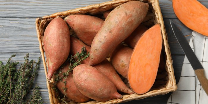 sweet potato in basket on wooden background, top view