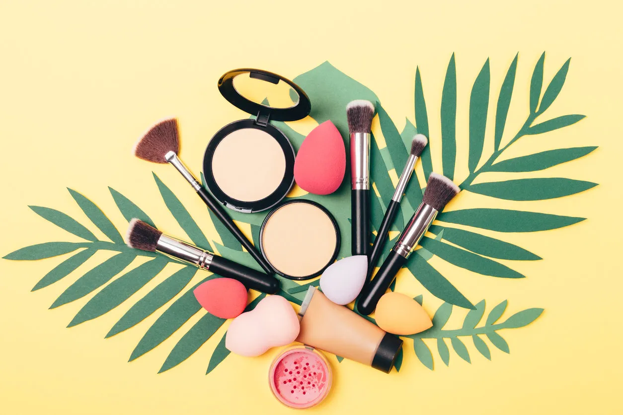 beauty makeup products and tools on palm leaves on yellow background, view from above