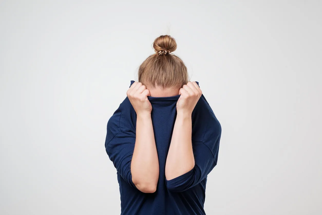 european woman hiding face under the clothes she is oulling sweater on her head depressed emotion wish to be alone