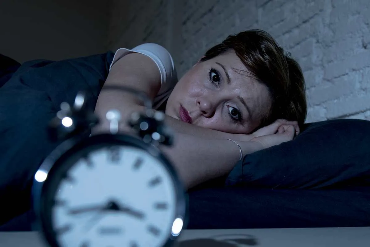 young attractive red haired caucasian woman lying in bed late at night trying to sleep suffering from insomnia, nightmares or sleeping disorders looking stressed and exhausted