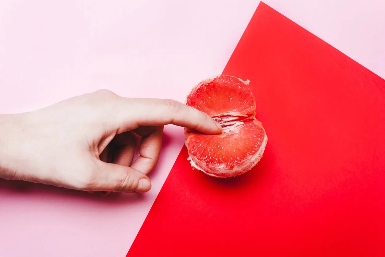 concept sex, masturbation hand, fingers in grapefruit, vagina symbol on a red background concept sex, masturbation hand, fingers in grapefruit, vagina symbol on a red background