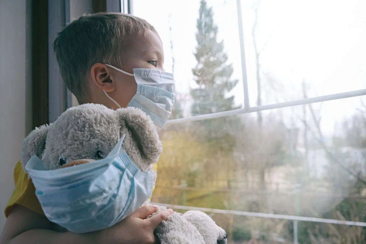 sad illness child on home quarantine boy and his teddy bear both in protective medical masks sits on windowsill and looks out window virus protection, coronavirus pandemic, prevention epidemic sad illness child on home quarantine boy and his teddy bear both in protective medical masks sits on windowsill and looks out window virus protection, coronavirus pandemic, prevention epidemic