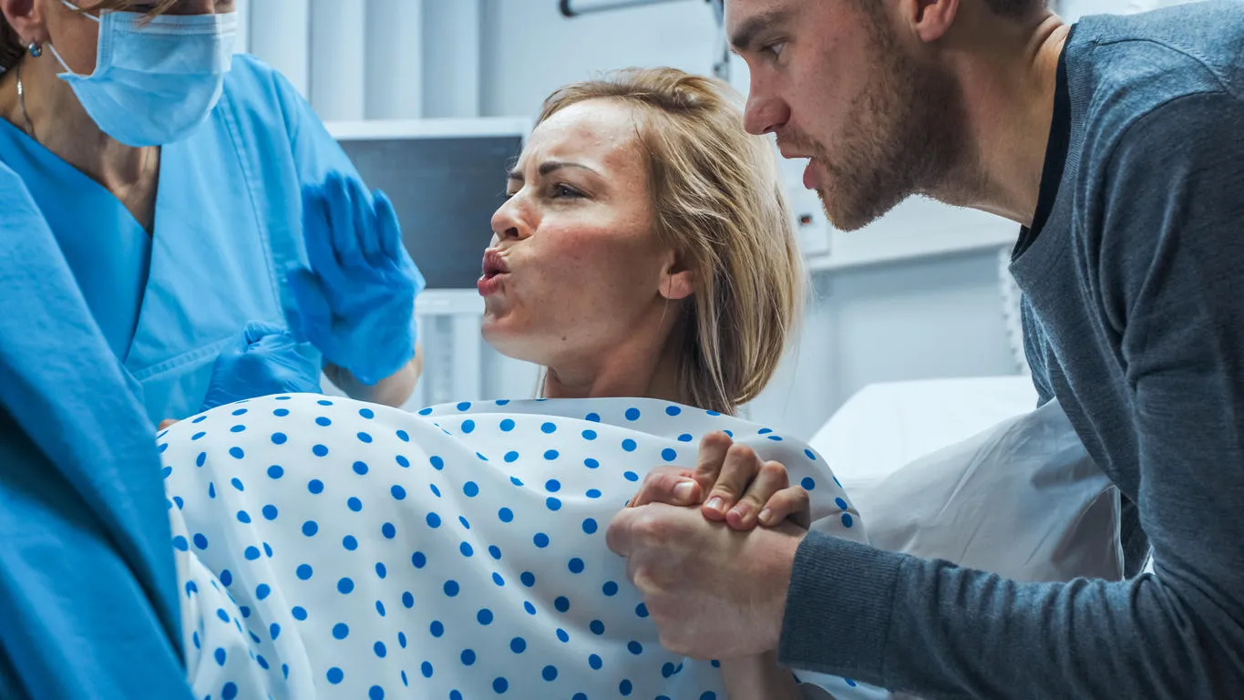 in the hospital, close-up on a woman in labor pushing hard to give birth, obstetricians assisting, spouse holds her hand modern maternity hospital with professional midwives in the hospital, close-up on a woman in labor pushing hard to give birth, obstetricians assisting, spouse holds her hand modern maternity hospital with professional midwives