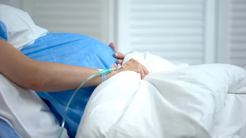 pregnant woman holding blanket, feeling abdominal pain, risk of miscarriage