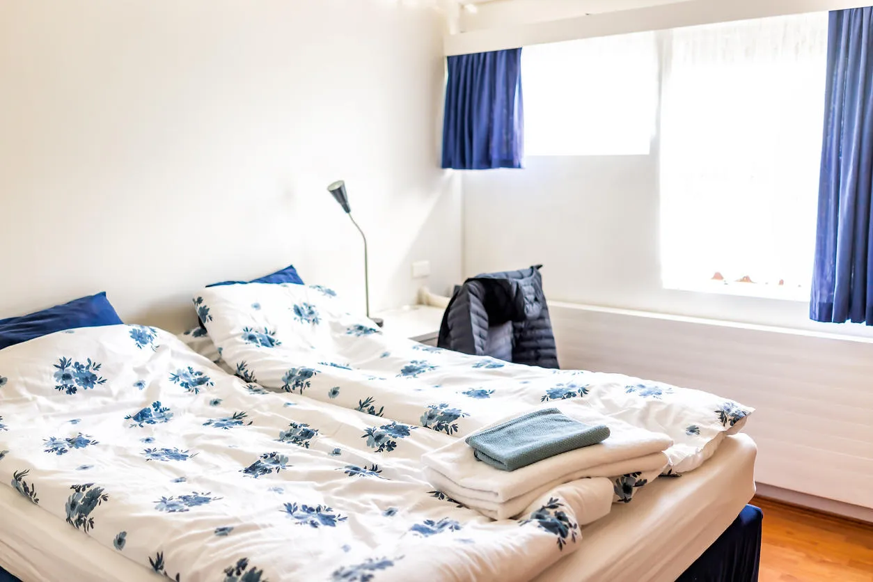 clean european double queen bed comforter with table lamps and decorative blue pillows in bedroom home house typical apartment towels in hostel hotel room