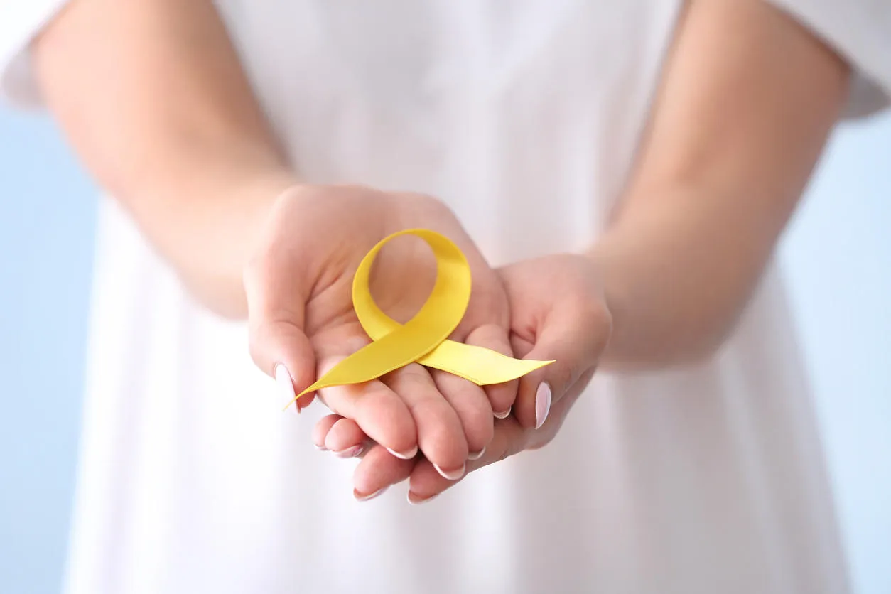 woman holding yellow ribbon, closeup cancer awareness concept woman holding yellow ribbon, closeup cancer awareness concept