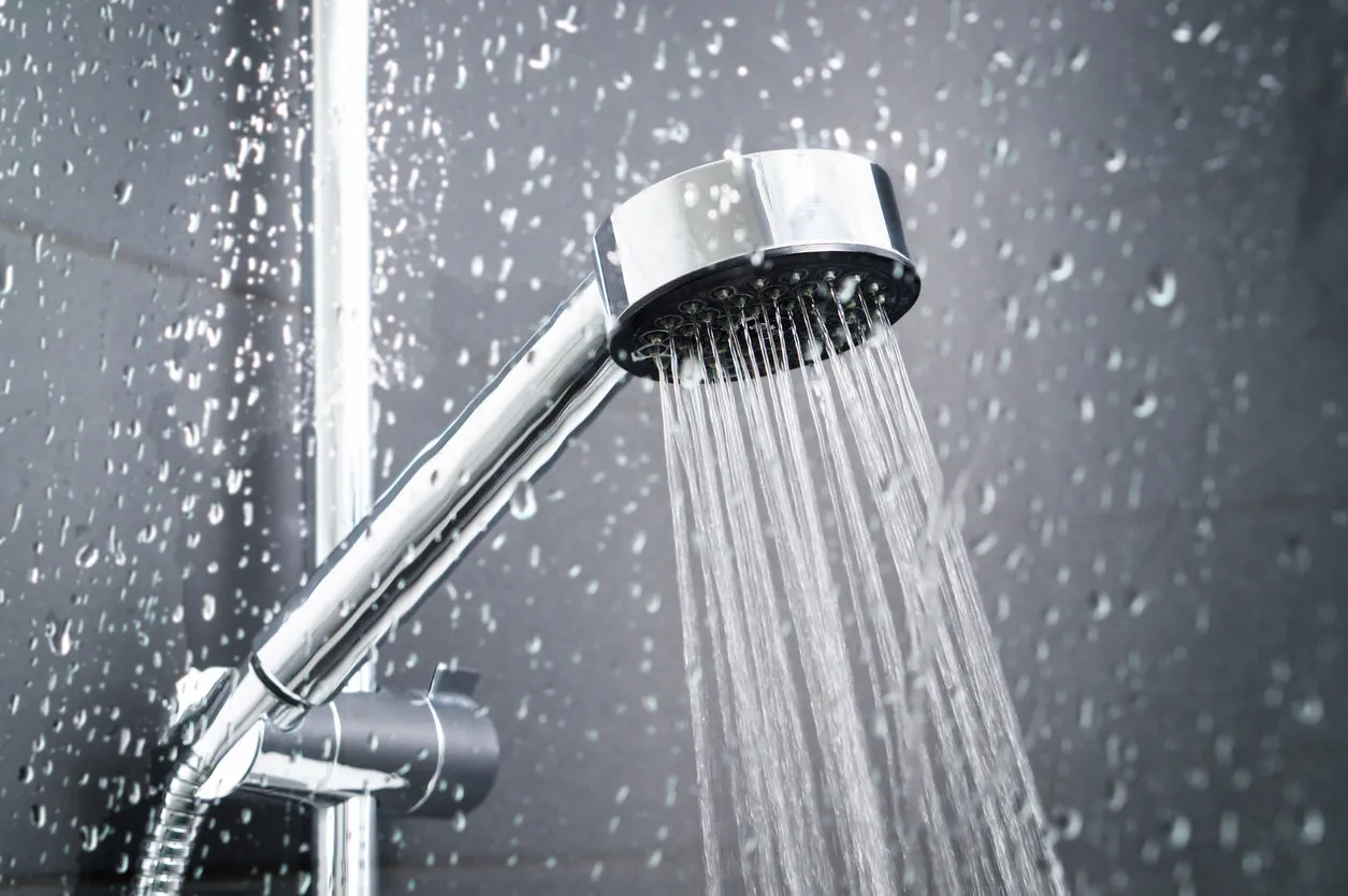 fresh shower behind wet glass window with water drops splashing water running from shower head and faucet in modern bathroom