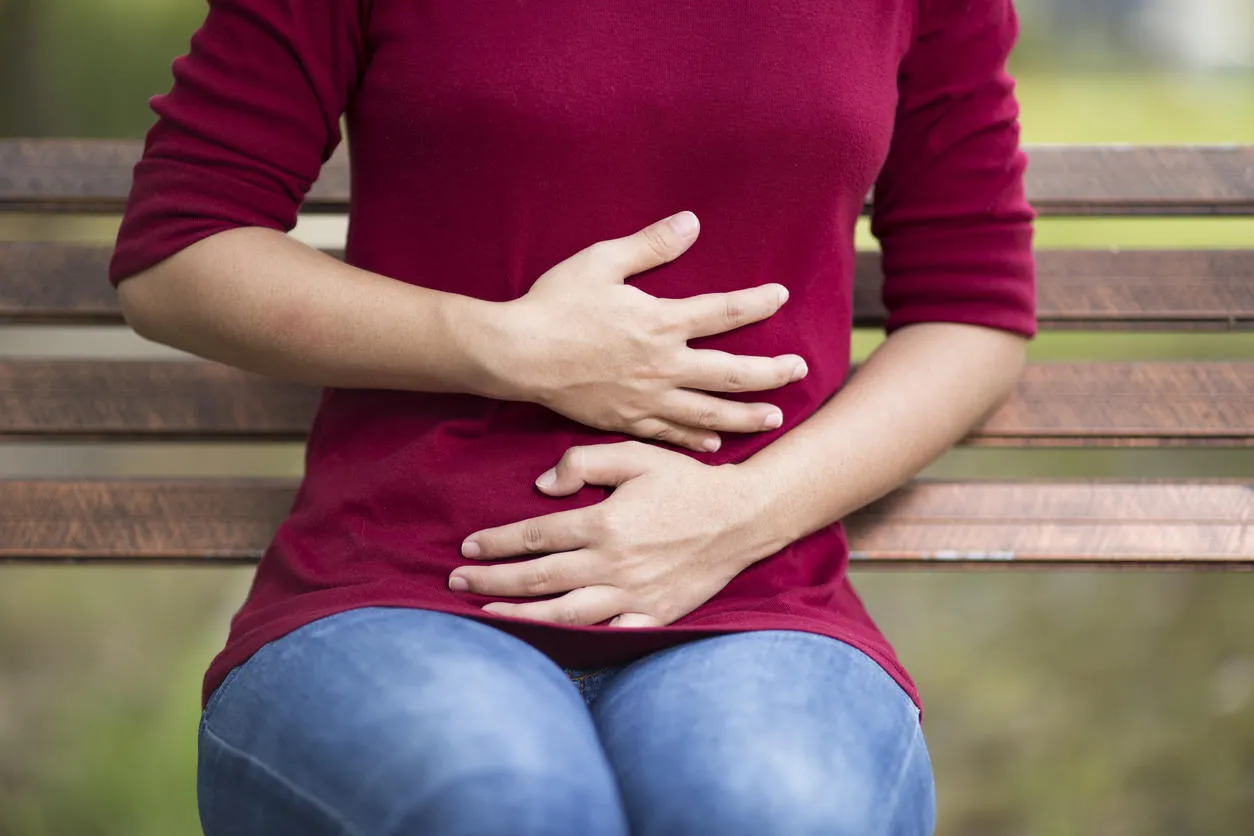 woman has stomach ache sitting on bench at park woman has stomach ache sitting on bench at park