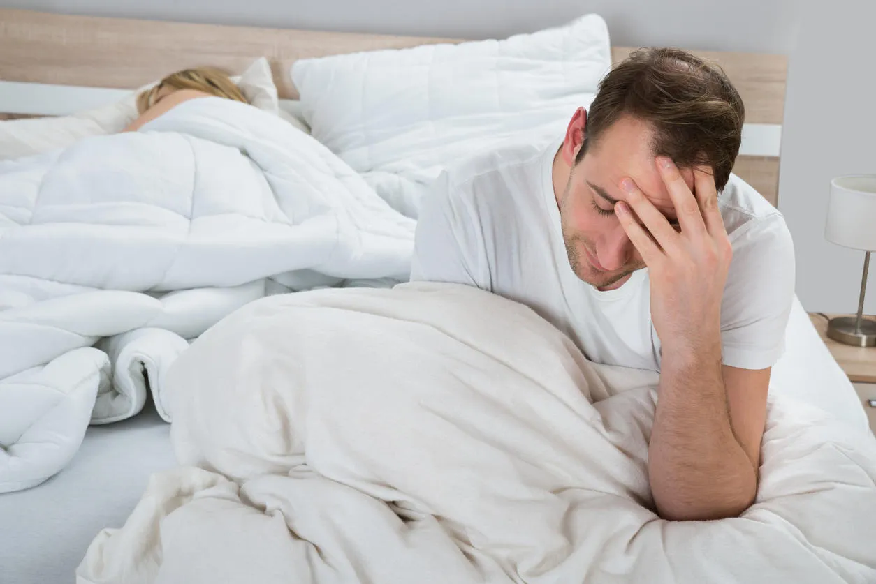 depressed man sitting on bed while woman sleeping in bedroom depressed man sitting on bed while woman sleeping in bedroom