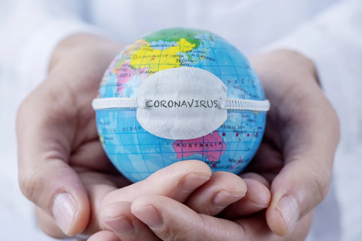 closeup of a caucasian doctor man holding a world globe with a protective mask with the word coronavirus written in it closeup of a caucasian doctor man holding a world globe with a protective mask with the word coronavirus written in it