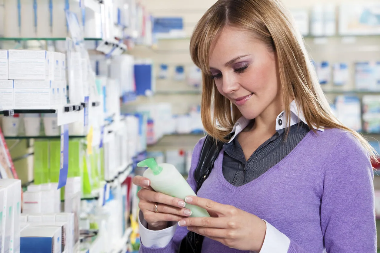 portrait of blonde woman reading label of shampoo in pharmacy copy space
