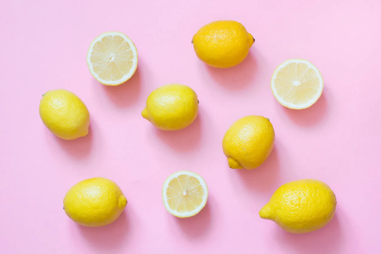 fresh whole and sliced lemon on punchy pink background flat lay