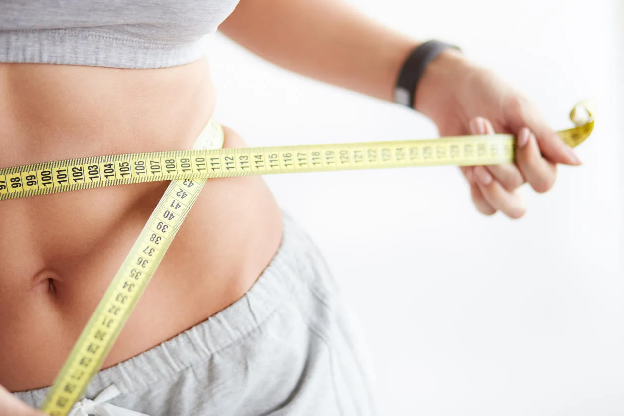bright closeup of slim young woman measuring her thin waist with a tape measure on white background bright closeup of slim young woman measuring her thin waist with a tape measure on white background