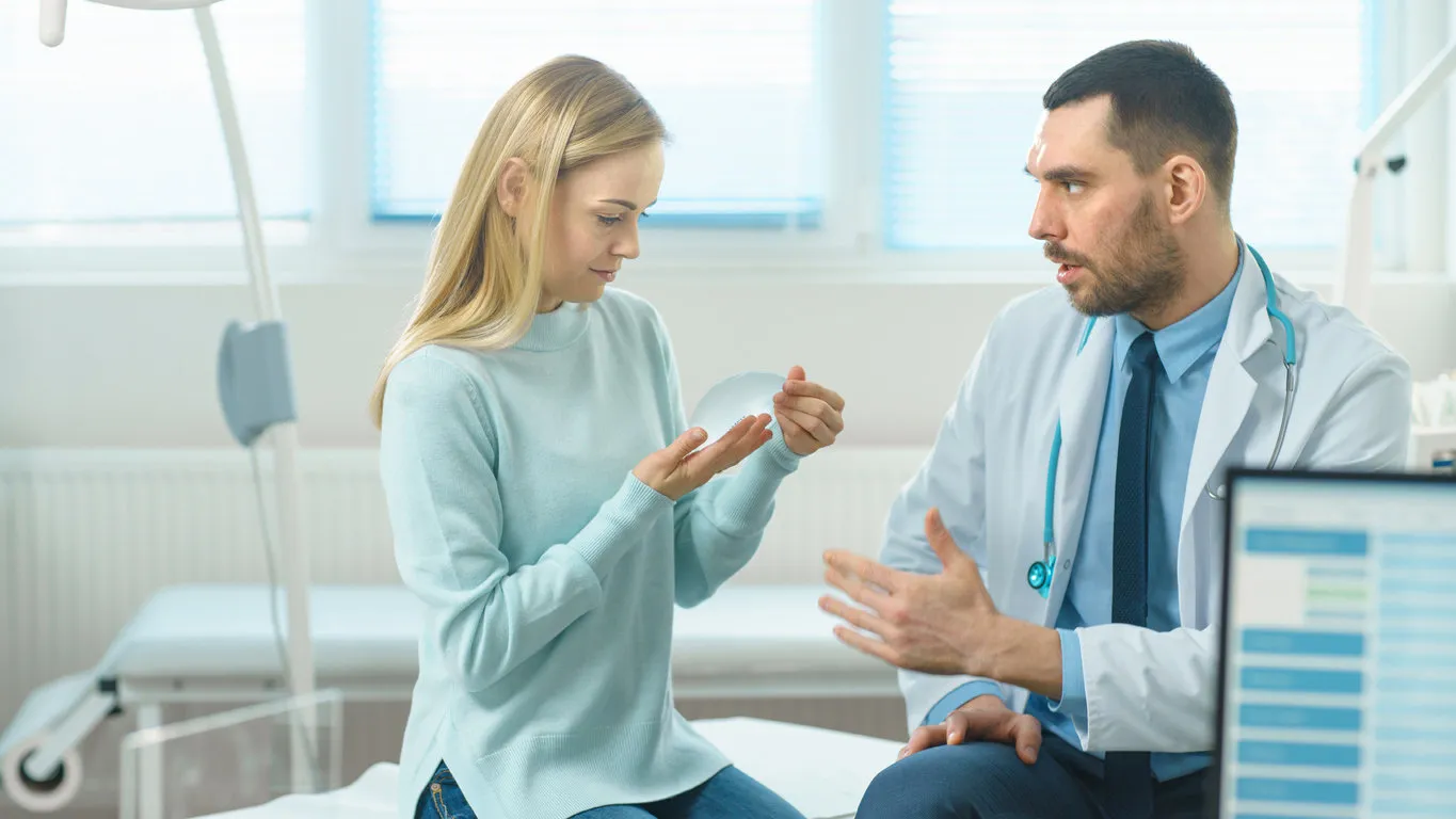 plastic   cosmetic surgeon shows female patient breast implant samples and talk about her future surgery modern hospital with technologically advanced medical equipment