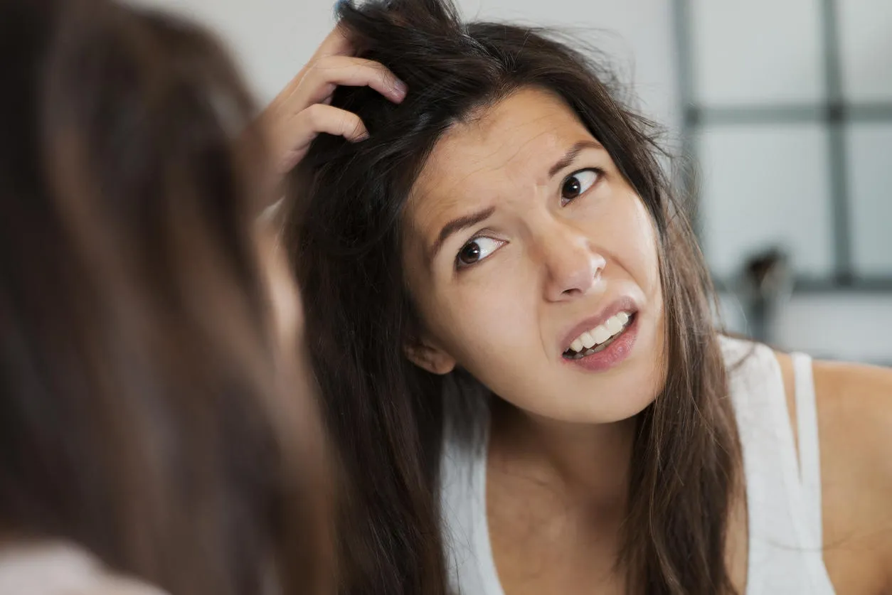 woman having a bad hair day grimacing in disgust as she looks in the mirror and runs her hands through her hair woman having a bad hair day grimacing in disgust as she looks in the mirror and runs her hands through her hair
