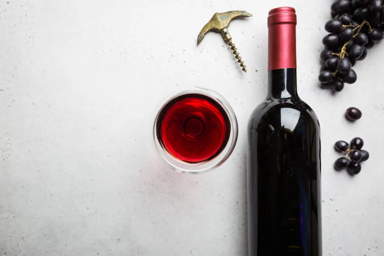 red wine in a glass and ripe grapes on white background, top view