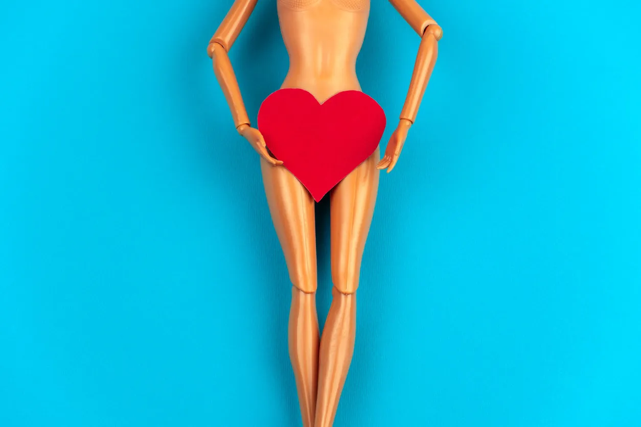 legs of a plastic doll with a red heart covering the crotch on a vibrant blue background legs of a plastic doll with a red heart covering the crotch on a vibrant blue background