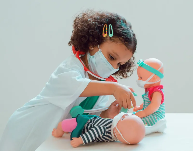 a little girl playing the doctor gives her patient an injection, they all wear protective masks a little girl playing the doctor gives her patient an injection, they all wear protective masks