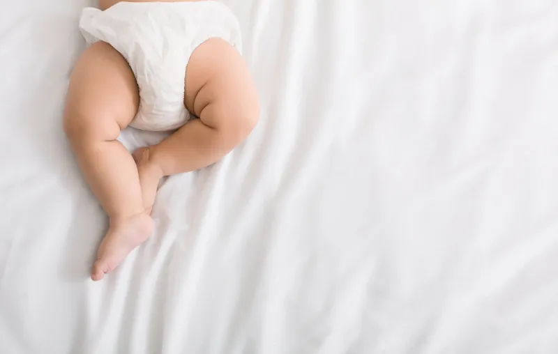 baby legs and bottom in diaper on white bed background, top view, copy space baby legs and bottom in diaper on white bed background, top view, copy space