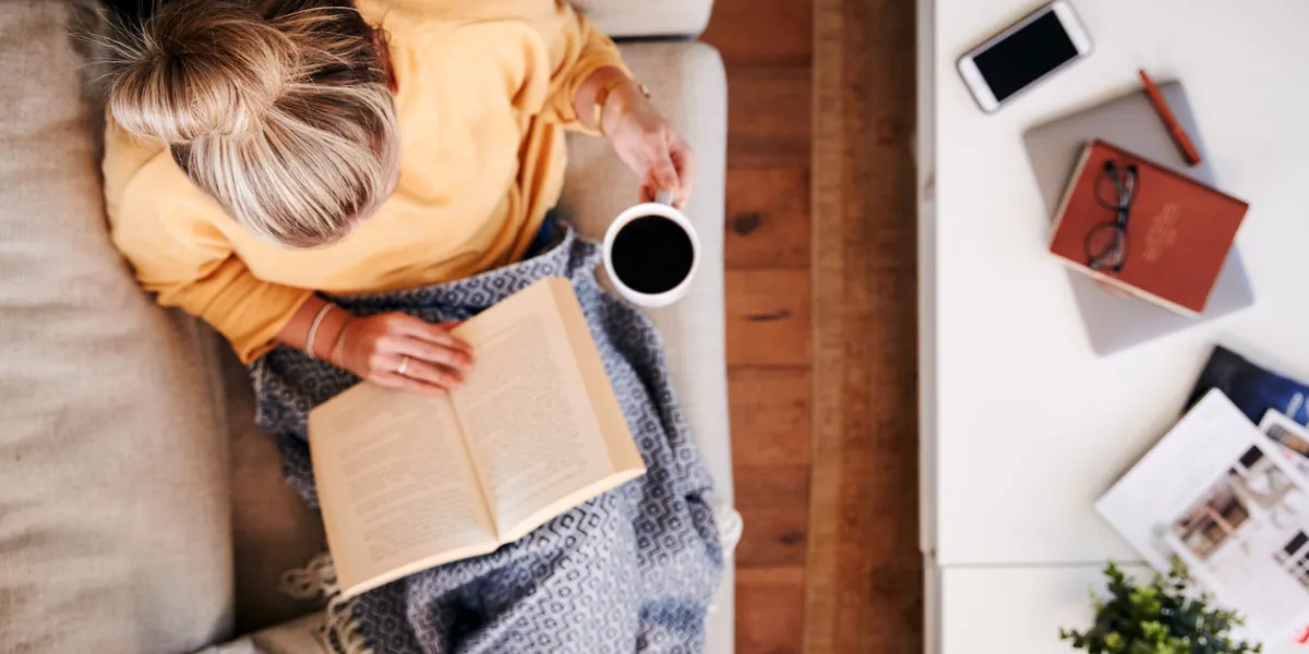 overhead shot looking down on woman at home lying on reading book and drinking coffee overhead shot looking down on woman at home lying on reading book and drinking coffee