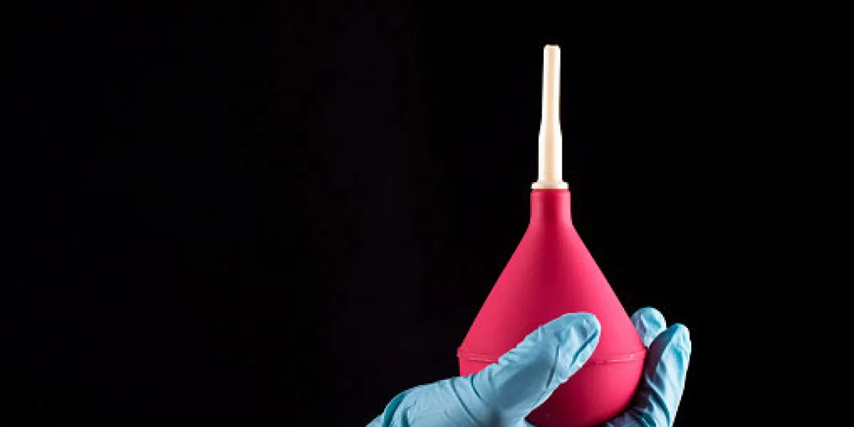 a gloved hand holds an enema on a black background