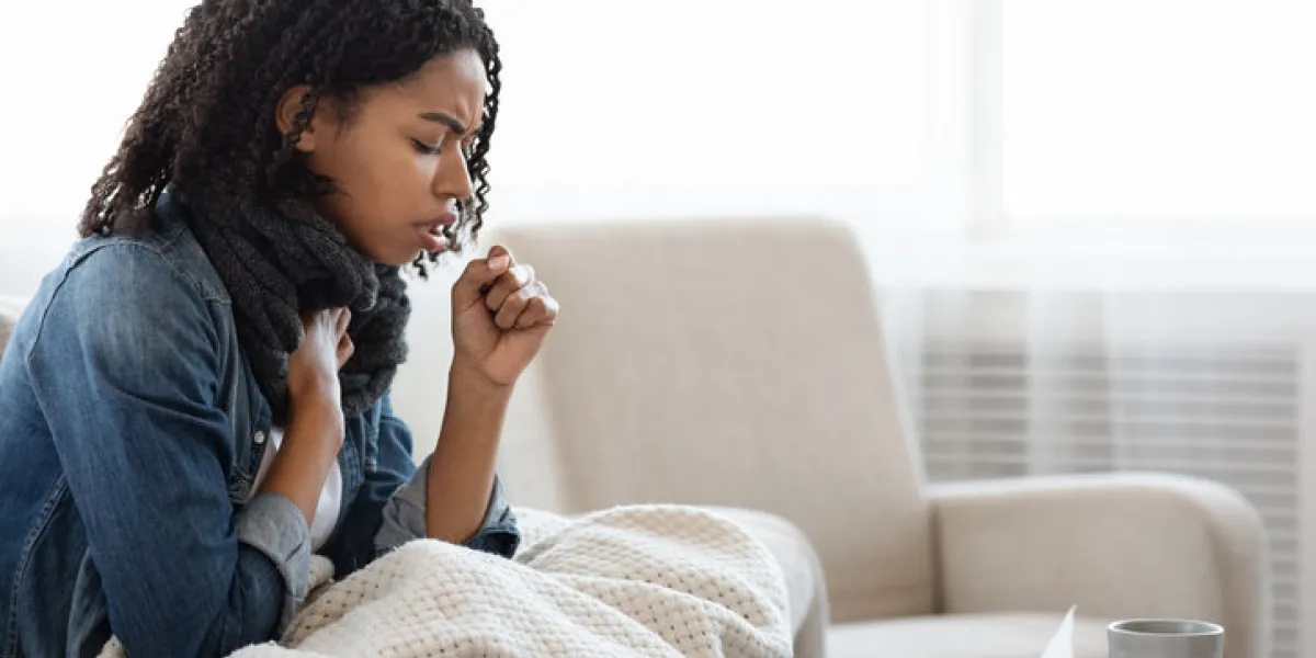 risk of coronavirus sick black woman coughing hard at home, sitting on couch wearing scarf and covered with blanket, side view with copy space risk of coronavirus sick black woman coughing hard at home, sitting on couch wearing scarf and covered with blanket, side view with copy space