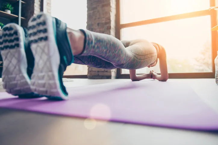 close up photo of sportswoman's sneakers athlete is holding plank position standing on elbows on purple carpet in class club gym view on window with sunlight, sunshine, reflection close up photo of sportswoman's sneakers athlete is holding plank position standing on elbows on purple carpet in class club gym view on window with sunlight, sunshine, reflection