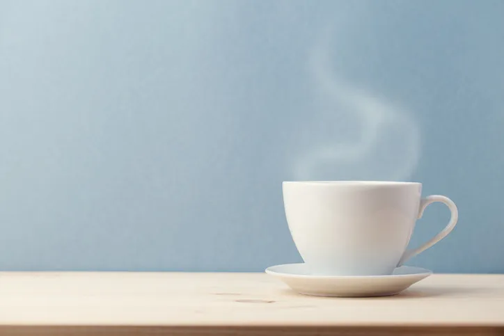 small white cup on saucer with steam coming from hot delicious drink on blue background