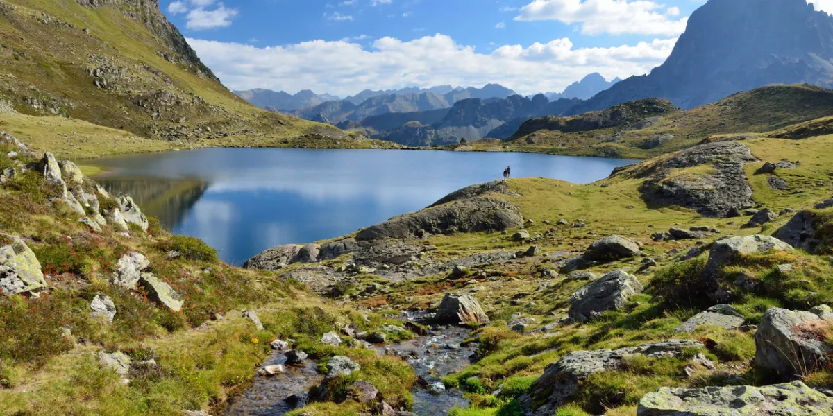 a mountain stream runs to the alpine lake gentau there are tourists and the recognizable summit pic du midi d'ossau in the background a mountain stream runs to the alpine lake gentau there are tourists and the recognizable summit pic du midi d'ossau in the background