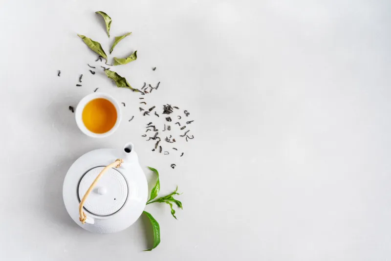 tea concept with white tea set of cups and teapot surrounded with fresh tea leaves on concrete background with copy space tea concept with white tea set of cups and teapot surrounded with fresh tea leaves on concrete background with copy space