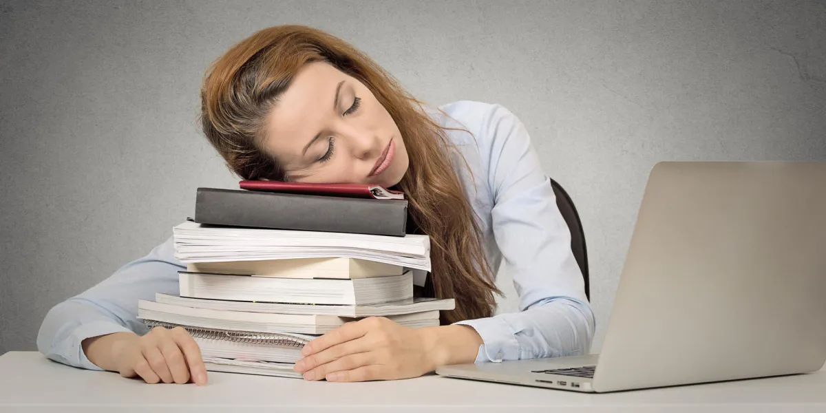 trop de travail femme fatiguée dormir sur des livres à son bureau en face de l'ordinateur isolé sur fond de bureau de mur gris horaire chargé au collège, lieu de travail, concept de privation de sommeil