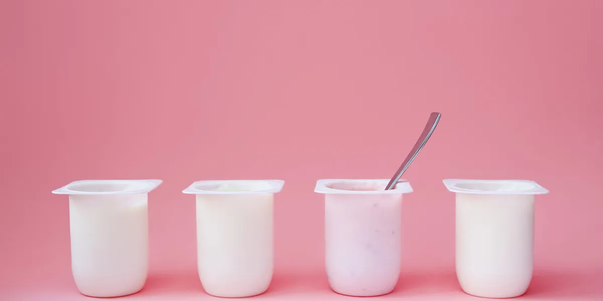 four yogurts in white plastic cups on pink background with copy space strawberry pink yoghurt with spoon in it minimal style concept of better choice four yogurts in white plastic cups on pink background with copy space strawberry pink yoghurt with spoon in it minimal style concept of better choice