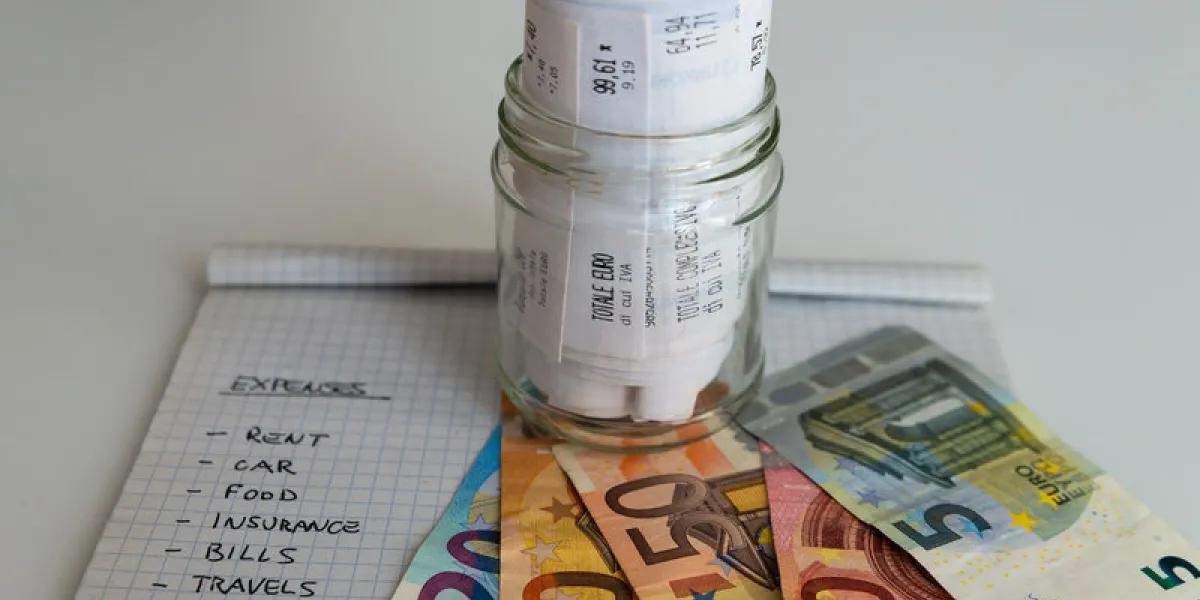 monthly budget notebook next to banknotes, coins and jar full of