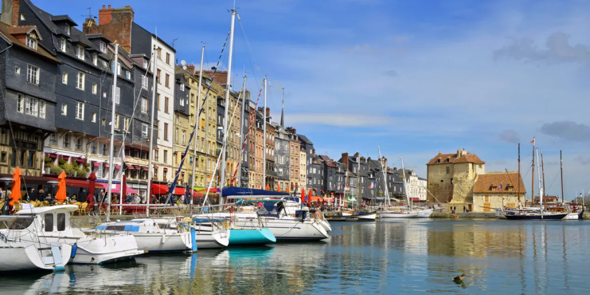 une vue sur le port de honfleur (14600) avec ses bateaux et ses reflets sous le soleil et le ciel bleu, dans le département du calvados en région normandie, france